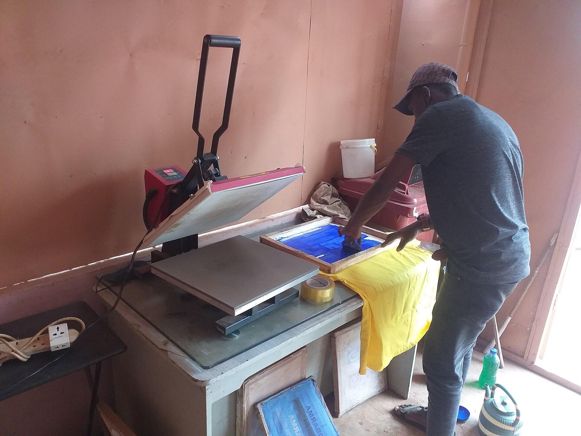 A printer working at a bench beside an open heat press